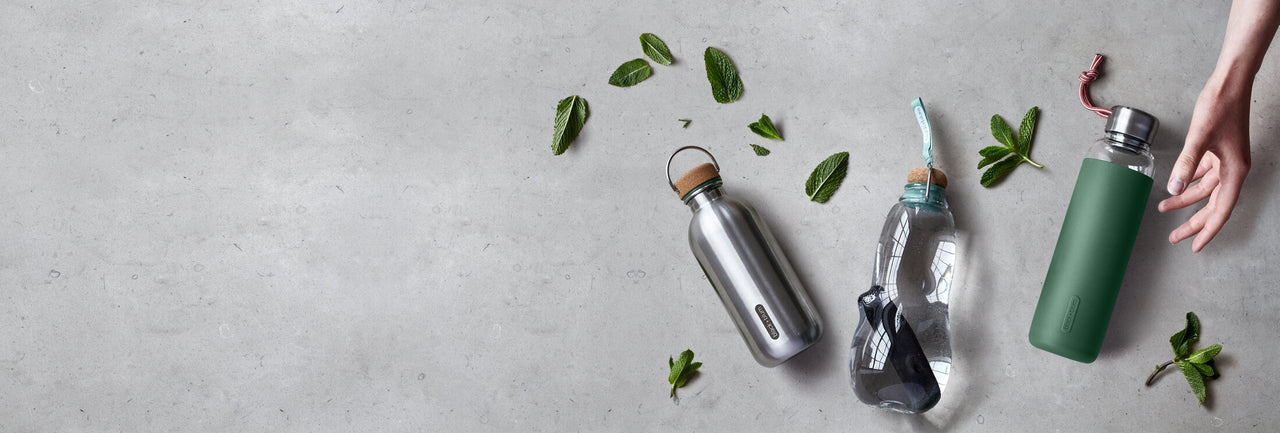 Reusable leak proof water bottles on gray bench with mint leaves