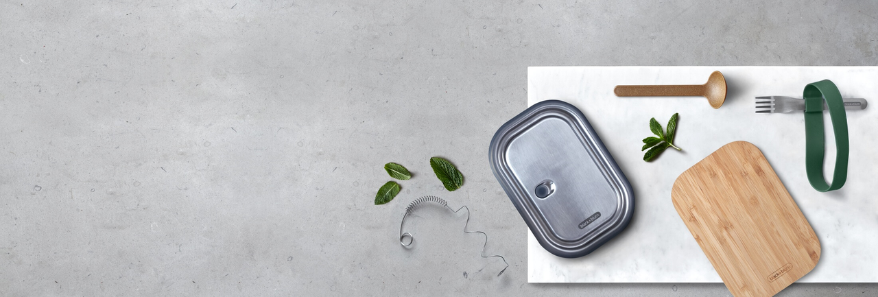 Replacement lids and spoons for reusable lunch boxes on a gray bench with marble chopping board